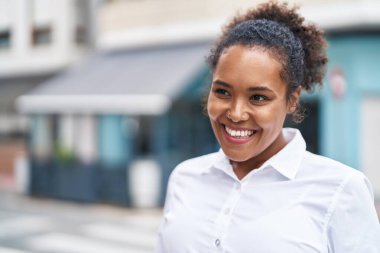 Afro-Amerikalı kadın gülümsüyor. Kendinden emin bir şekilde caddeye bakıyor.
