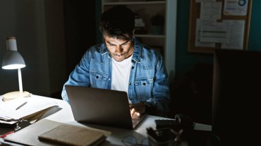 Masa lambası, belgeler ve gözlüklerle karanlık ofiste dizüstü bilgisayarda çalışan İspanyol bir adam.