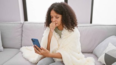 Evdeki kanepede oturan hasta, genç ve güzel bir İspanyol kadın. İnternetteki tıp uzmanlarına mesaj atmak ya da danışmak için akıllı telefonunu kullanıyor.