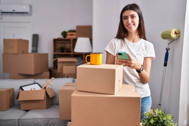 Genç, güzel, İspanyol bir kadın akıllı telefon kullanıyor. Yeni evinde kahve içiyor.