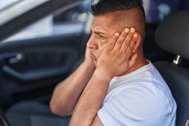 Young latin man stressed driving car at street