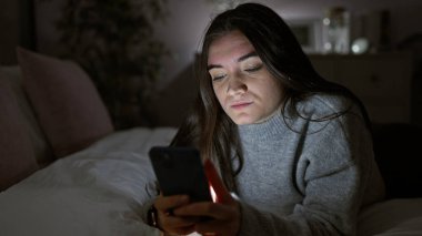 Geceleri karanlık yatak odasında akıllı telefon kullanan İspanyol kadın..