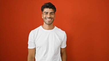 Sakallı yakışıklı genç adam, kırmızı izole edilmiş arka plana gülümsüyor..