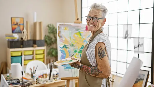 Zelfverzekerde Grijsharige Seniorenkunstenares Glimlachend Terwijl Haar Vertrouwde Penseel Palet Vasthoudt — Stockfoto