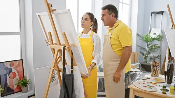 In an art studio, a man and woman artists decked in aprons, intently looking at the drawing they\'ve created together
