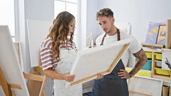 stock image A man and woman artist team collaboratively reviewing a canvas in a bright studio setting.