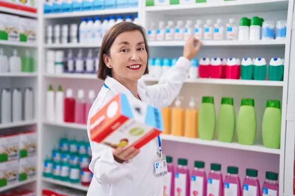 Mujer Mediana Edad Farmacéutico Sonriendo Confiado Sosteniendo Paquete Vitaminas Farmacia — Foto de Stock