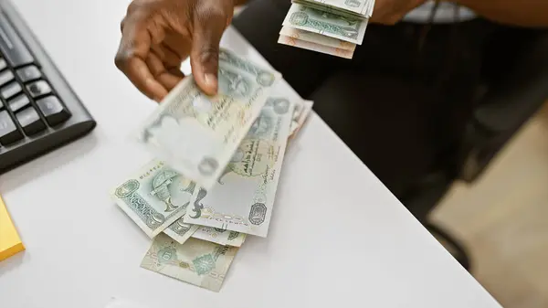 African woman counting uae dirhams in a modern office setting, showcasing currency, work, and ethnicity.