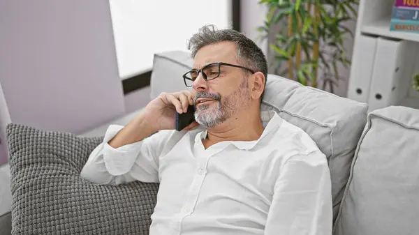 Gri saçlı, yorgun, genç İspanyol bir adam ciddi bir telefon konuşmasına dalmış, evdeki oturma odasındaki kanepeye yığılmış.