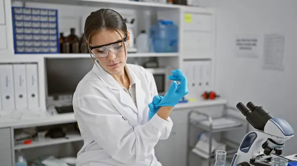 In the heart of science, young, beautiful hispanic woman scientist, wearing gloves, carrying a serious expression on her face while working diligently in a bustling laboratory.