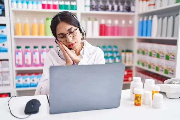 Young arab woman working at pharmacy drugstore using laptop sleeping tired dreaming and posing with hands together while smiling with closed eyes.