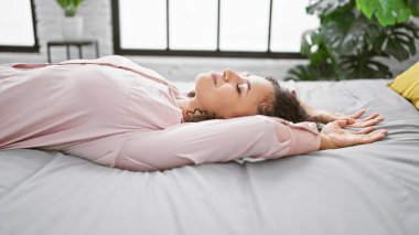Uyanık ve enerjik, güzel İspanyol kadın yatakta kollarını açıyor, rahat yatak odasında rahatlıyor.