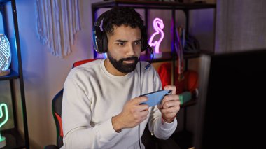 Geceleri oyun odasında cep telefonu kullanan sakallı İspanyol bir adam, odaklanmışa benziyor.