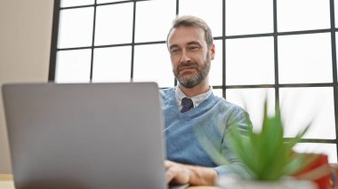 Ofiste sakallı, orta yaşlı yakışıklı bir adam. Pencere kenarına dizüstü bilgisayar kullanıyor.