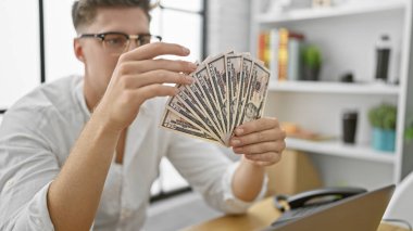 Yakışıklı beyaz iş adamı ofisinde oturmuş, ciddi ciddi dolar banknotlarını sayıyor, başarılı bir yatırım başarısı.!