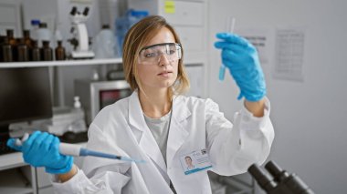 Yoğun bir adanmışlık, genç, çekici sarışın kadın bilim adamı son teknoloji tıbbi araştırma laboratuvarında yapılan önemli bir deney sırasında bir deney tüpüne sıvıyı ustalıkla döküyor..