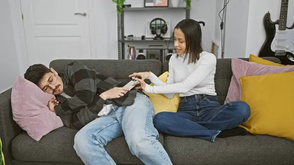 stock image Woman taking smartphone from sleeping man on sofa in living room with guitar