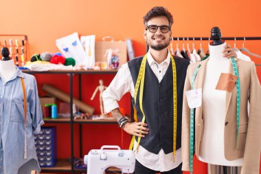 Genç İspanyol terzi gülümsüyor Atölyede kendine güvenen manikine yaslanıyor