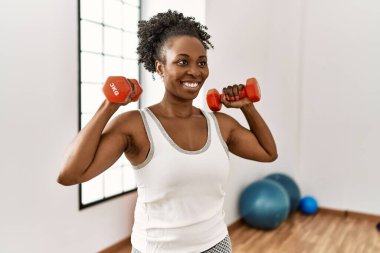 Spor merkezinde dambılları kullanarak gülümseyen Afrikalı Amerikalı kadın.