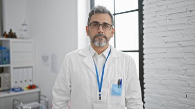 Yakışıklı, gri saçlı genç İspanyol bilim adamı canlı bir laboratuarda, çalışma masasında dururken mikroskopla analiz üzerine yoğunlaşarak ciddi şekilde tıbbi deneylere odaklanmış.