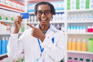 Eczanede çalışan Afrikalı kadın elinde kredi kartıyla elini ve parmağını göstererek mutlu mesut gülümsüyor. 