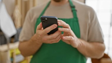 Bulanık bir odada akıllı telefon kullanan önlük giyen genç sakallı bir adam..