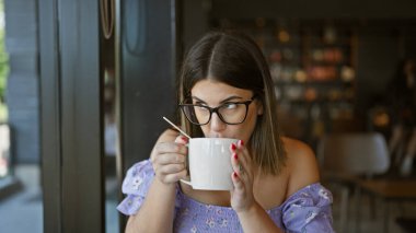 Gözlüklü güzel İspanyol kadın rahat bir kafe masasında sıcak bir fincan kahvenin tadını çıkarıyor. Yoğun sabahına biraz ara veriyor.