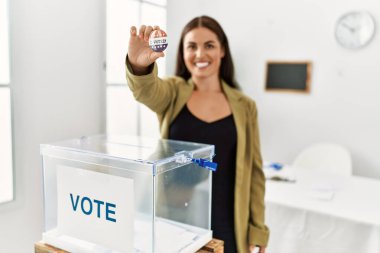 Young beautiful hispanic woman electoral table president holding vote badge at electoral college
