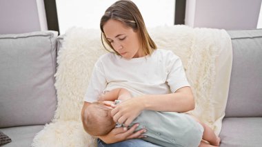 Evde sevgi dolu bir anne, sevgi dolu bir aile kanepesinde oturuyor, bebeğini emziriyor, bu samimi annelik anının tadını çıkarıyor, bebeğe besleyici anne sütü sunuyor.