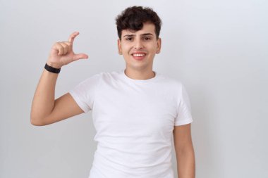 Gündelik beyaz tişört giyen, gülümseyen, kendine güvenen, el hareketi yapan, parmaklarıyla işaret yapan ve kameraya bakan iki kişilik olmayan genç bir adam. ölçüm kavramı. 