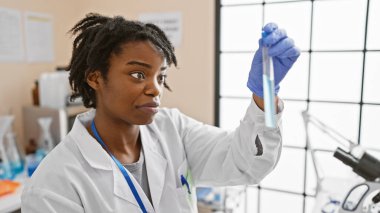 Parlak bir laboratuvar ortamında test tüpünü analiz eden Afrikalı bir bilim kadını..