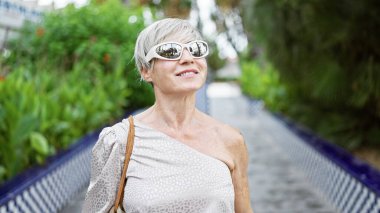 Kendine güvenen olgun bir kadın, serin bir parkta yemyeşil bir havayla çevrili açık havada güneşli bir günün tadını çıkarır..