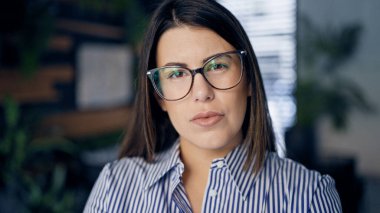 Genç, güzel, İspanyol bir kadın. Ofiste ciddi yüzlü gözlük takıyor.