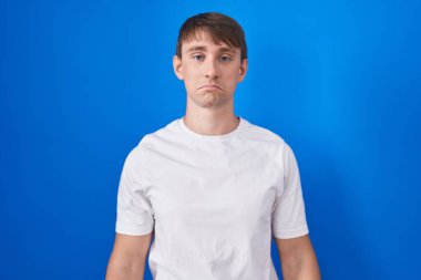 Mavi arka planda duran beyaz, sarışın bir adam depresyonda ve üzüntüden ağlıyor, kızgın ve korkmuş. hüzünlü ifade. 