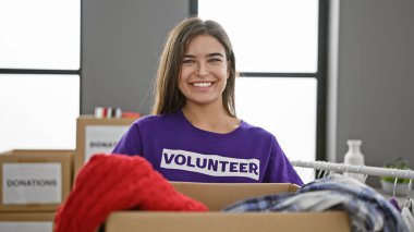 Kendine güveni tam genç İspanyol bir kadın, güzel gülümsüyor, hayır kurumunda kıyafet paketiyle gönüllü çalışıyor.