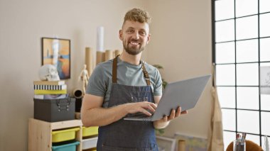 Yaratıcı bir stüdyoda sakallı yakışıklı bir genç dizüstü bilgisayar tutuyor..