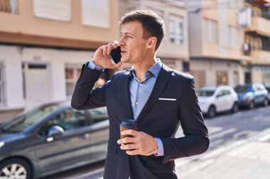 Young man business worker talking on smartphone drinking coffee at street
