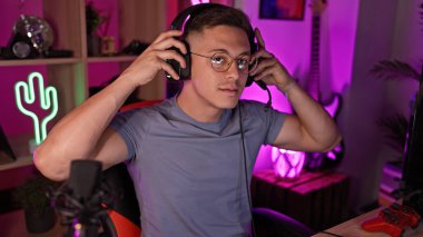 Yakışıklı İspanyol bir adam geceleri neon ışıklı bir oyun odasında kulaklıklarını ayarlıyor, çağdaş bir iç mekan dekorunu canlandırıyor..