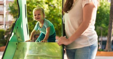 Anne ve oğlu parkta kayak yaparken kendinden emin bir şekilde gülümsüyor.