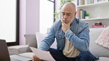 Düşünceli bir İspanyol, rahat bir oturma odasında dizüstü bilgisayarındaki belgeleri inceliyor..