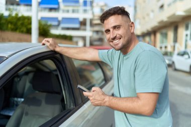 Young hispanic man using smartphone leaning on car at street