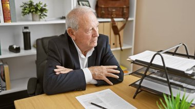 Ciddi bir kıdemli adamın büyüleyici portresi, başarılı bir iş adamı, ofiste odaklanmış bir bakışla oturuyor, kolları iş yerinde olgun bir özgüvenin timsali oldu.. 