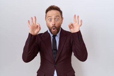 Sakallı, kravatlı, şaşırmış ve şaşırmış görünen orta yaşlı iş adamı parmaklarıyla onay sembolü yapıyor. çılgın ifade 