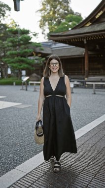 Neşeli, kendine güvenen İspanyol bir kadının büyüleyici görüntüsü, gözlükleriyle ışıldayan bir gülümseme, rastgele poz verip Kyoto, Japonya 'daki ikonik fushimi inari-taisha' ya doğru yürüyor..