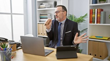 Olgun, gri saçlı iş adamı neşeli bir şekilde şarkıya başlıyor, ofisinde özenle çalışıyor, pozitif enerji yayıyor.