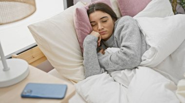 Genç bir İspanyol kadın rahat bir yatak odasında huzur içinde uyuyor. Yanında da akıllı bir telefon var.