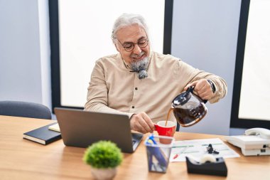 Orta yaşlı, kır saçlı, iş adamı. Ofiste fincana kahve dolduruyor.
