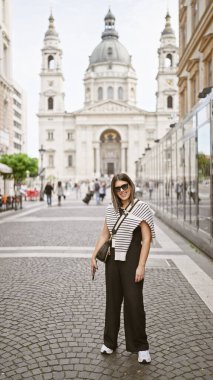 Budapeşte 'de bir kaldırım taşı caddesinde St. Stephen Bazilikası' nın önünde poz veren gülümseyen genç bir kadın..