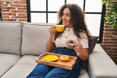 Genç, güzel, İspanyol bir kadın kahvaltısını evde, koltukta yapıyor.