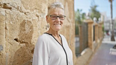 Neşeli, gri saçlı, kendinden emin, güneşli şehir sokağında dikilen, şehir hayatının tadını çıkaran son sınıf öğrencisi.